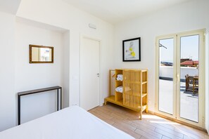 Ein Schlafzimmer mit einem Bett, einer Holzablage mit Handtüchern, einem gerahmten Bild und einer Schiebetür zu einem Außenbereich.