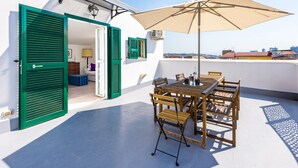 An outdoor patio with a table and chairs, a large umbrella, and green shutters on a white building. - Viewsuvio Two Apartments & Terraces (Naples)