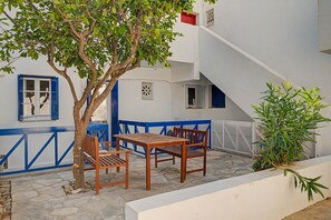 Eine Terrasse mit Tisch und Stühlen, ein Baum und ein weißes Gebäude mit blauen Akzenten.