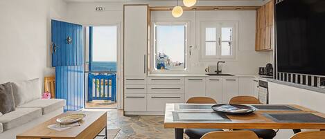 A modern kitchen with white cabinets, a black countertop, and a view of the sea through the open door.