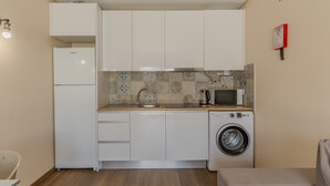 A compact kitchen with white cabinets, a washing machine, a microwave, and a sink. - #390 New Town Apartment with Shared Pool (Albufeira)