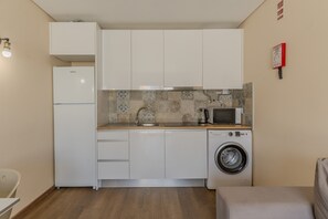 Eine kleine Küche mit weißen Schränken, einer Waschmaschine, einer Mikrowelle und einem Spülbecken.