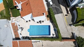 Ein Pool auf dem Dach mit einer Steindeck, umgeben von einem weißen Zaun, neben einem Gebäude mit roten Ziegeldach.