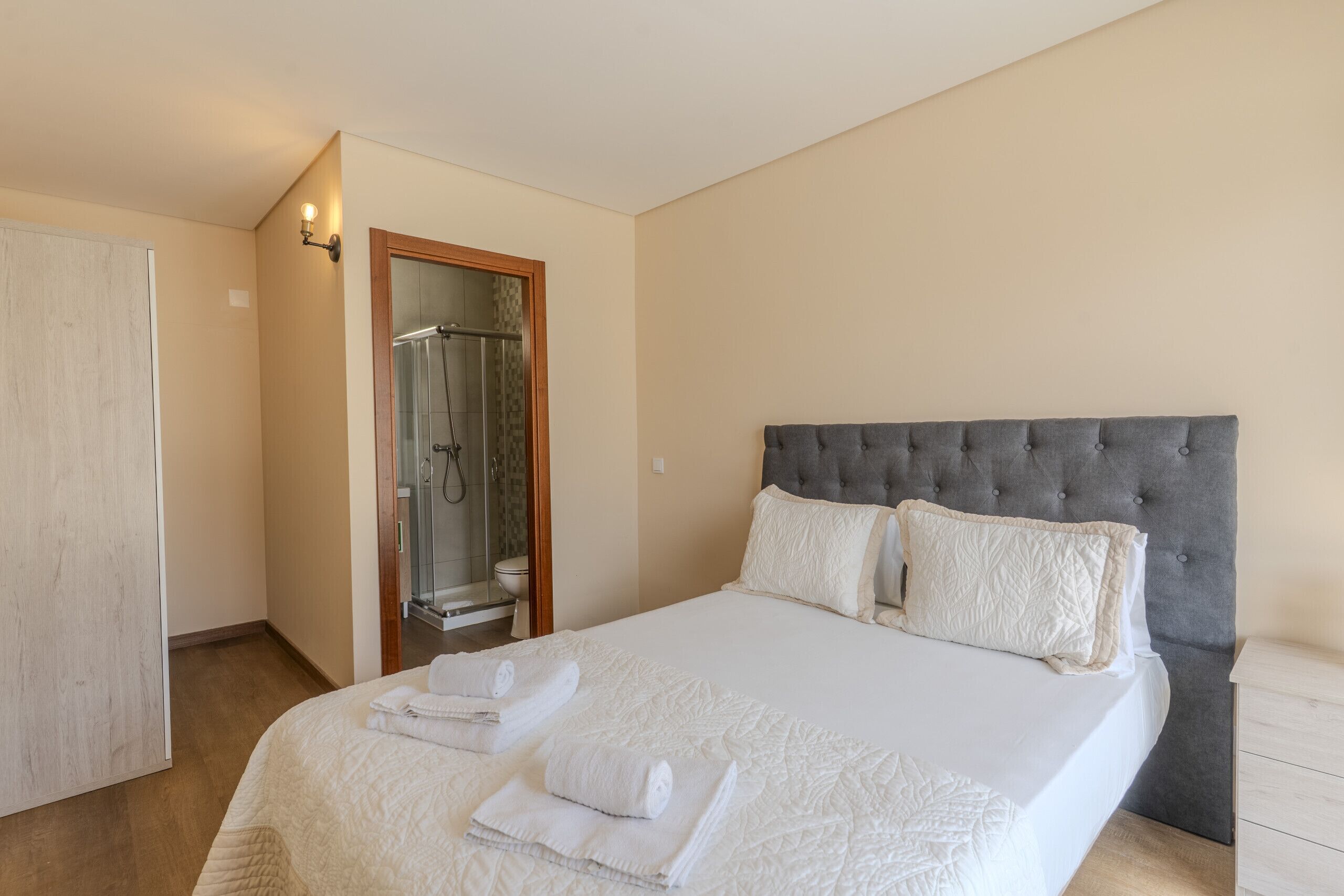 Un dormitorio con una cama grande, un cabecero tapizado en gris y una cabina de ducha con mampara de vidrio.