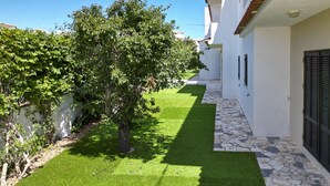 A narrow pathway with artificial grass, a tree, and white buildings with stone flooring. - #390 New Town Apartment with Shared Pool (Albufeira)