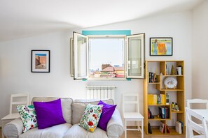 A living room with a sofa, chairs, a bookshelf, and a window with open shutters. - Viewsuvio Family Terrace (Naples)