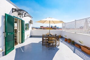 A rooftop terrace with a table and chairs, potted plants, and a white fence. - Viewsuvio Family Terrace (Naples)