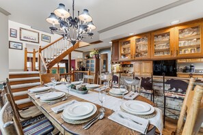 A dining area with a wooden table set for six, a chandelier, and wooden cabinets with glassware. - Downtown Breck Retreat| Deck + Trails + Hot Tub (Breckenridge)