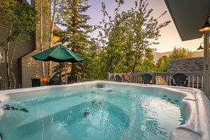 A hot tub with a green umbrella, surrounded by trees and a deck with chairs. - Downtown Breck Retreat| Deck + Trails + Hot Tub (Breckenridge)