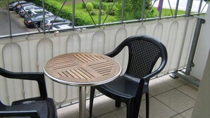 A balcony with a table and two chairs, a railing, and a view of parked cars and greenery. - 2 Person Holiday Park Home in Friedrichroda OT Finst (Friedrichroda)