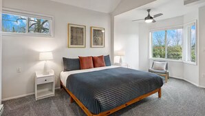 Una camera da letto con un letto, due comodini, una sedia, una ventola a soffitto e due finestre.