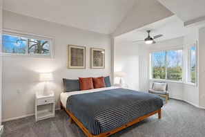 A bedroom with a bed, two bedside tables, a chair, a ceiling fan, and two windows. - The Dale Home (Seattle)