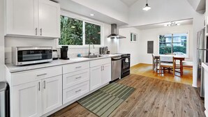 Una cucina moderna con mobili bianchi, forno integrato, microonde e macchina del caffè. È presente un'area pranzo con tavolo e sedie, e una finestra che offre vista all'esterno.