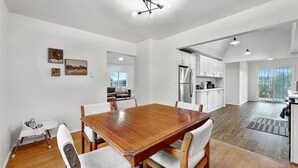 Un'ampia sala da pranzo con tavolo e sedie in legno, una cucina con mobili bianchi e vista attraverso una porta vetrata.