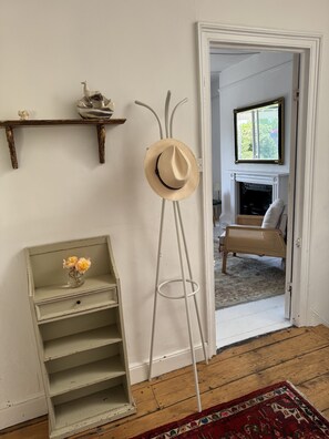 A room with a wooden floor, a standing hat rack, a small shelf with flowers, and a doorway leading to another room with a fireplace. - Superb Hastings Old Town Duplex with parking and sea views (Hastings)