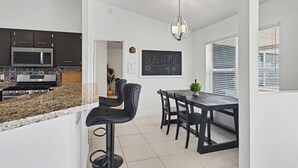 A modern kitchen with dark cabinets, a granite countertop, a stainless steel stove, and a bar stool. - Cozy Carribean/Mediterranean Home in Kissimmee, FL (Kissimmee)