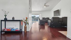 A modern living room with a wooden floor, a black console table, a vase with flowers, and a seating area with sofas. - Cozy Carribean/Mediterranean Home in Kissimmee, FL (Kissimmee)