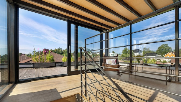 Un interior moderno con ventanas amplias, una terraza de madera y una escalera.