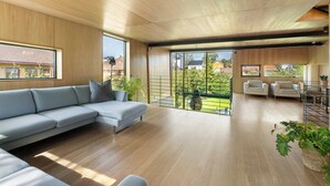 Una sala moderna con un sofá seccional, una zona de comedor con mesa y sillas, y ventanas grandes que ofrecen vistas al exterior.
