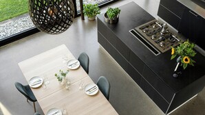 Una cocina moderna con estufa a gas integrada, una mesa de comedor preparada para cuatro personas y una planta en maceta sobre la encimera.