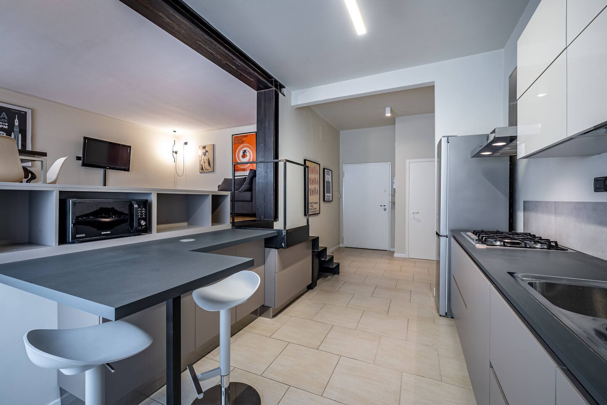 Una cucina moderna con piano cottura integrato, televisore e sgabelli da bar.