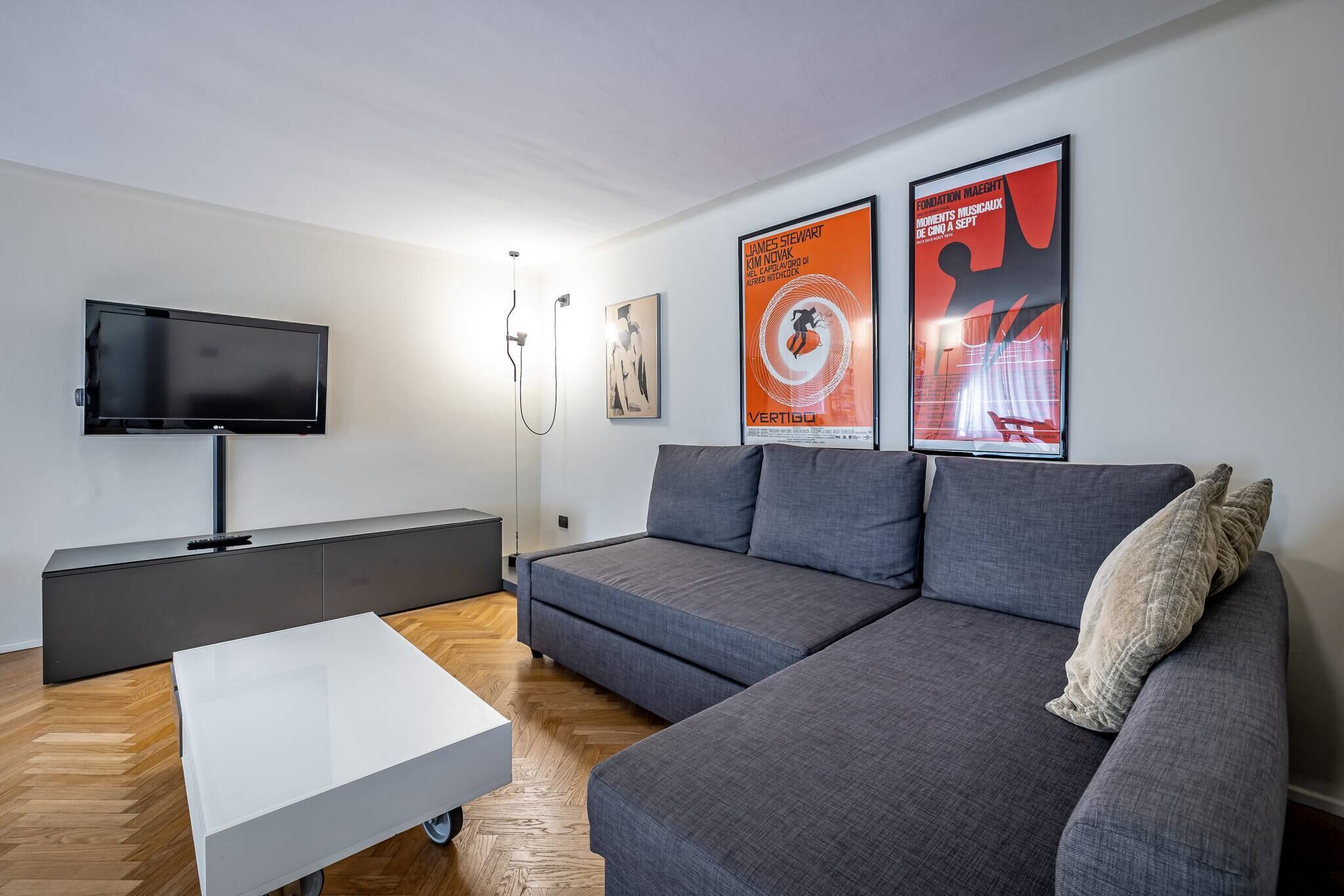 Un salon moderne avec un canapé gris, une table basse blanche et un téléviseur à écran plat posé sur un meuble.