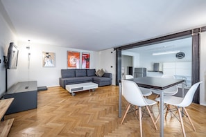 En moderne stue med en grå sofa, et sofabord og et spiseområde med hvide stole.