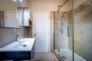 Une salle de bain moderne avec une douche en verre, un lavabo blanc et une porte donnant sur une autre pièce.