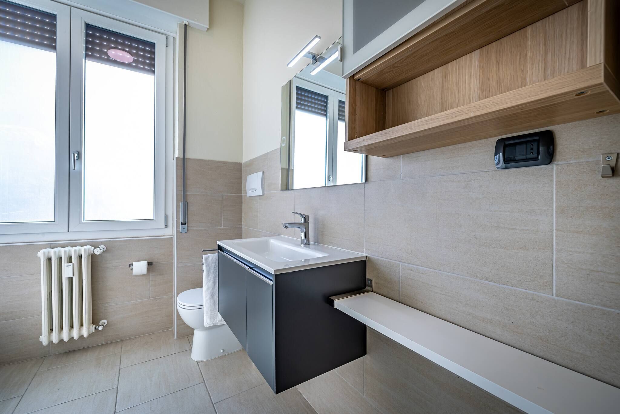 Une salle de bain moderne avec un lavabo intégré, des toilettes, un radiateur et une fenêtre.