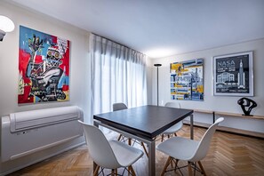 Un espace de salle à manger moderne, avec une table et des chaises, une grande peinture abstraite et deux affiches encadrées accrochées au mur.