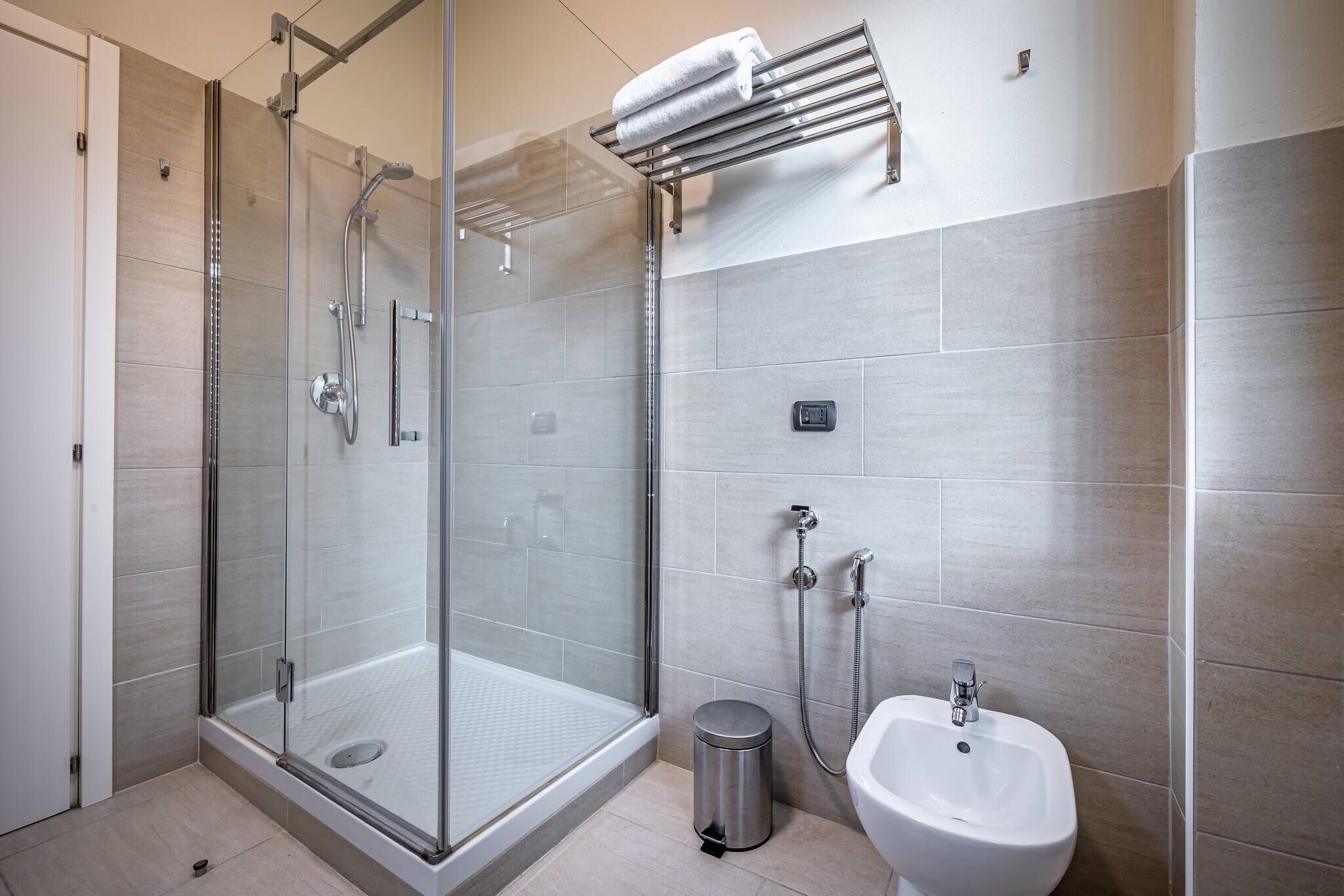 A modern bathroom with a glass-enclosed shower, a white sink, and a towel rack.