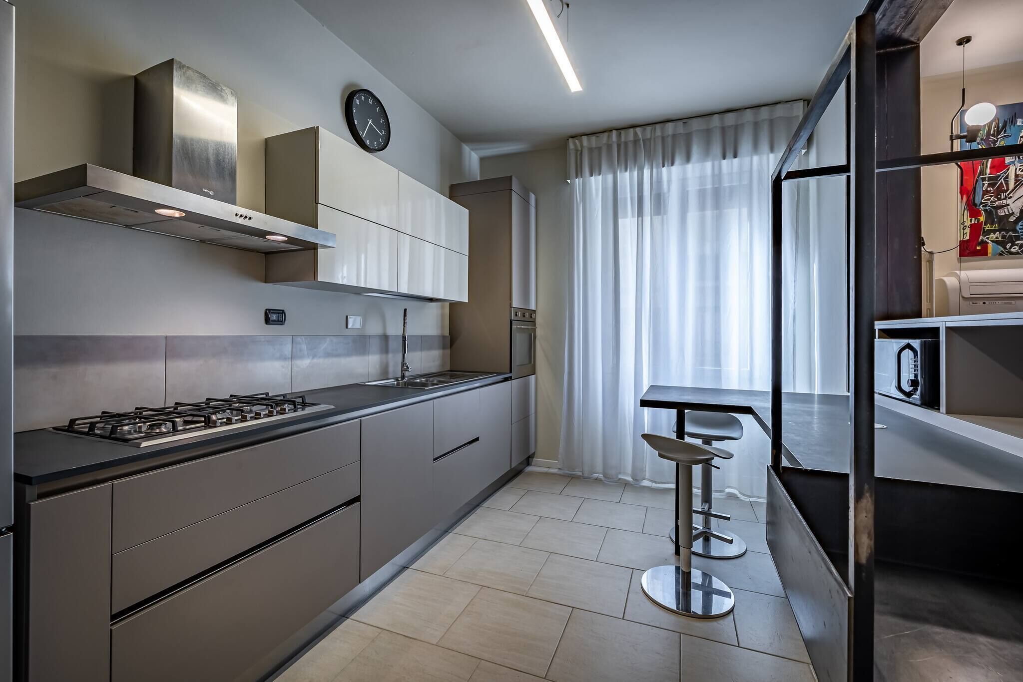Una cocina moderna con estufa a gas, campana de acero inoxidable y un reloj en la pared.