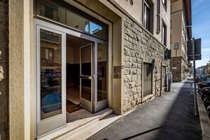 Un immeuble avec une façade en pierre, une entrée en verre et un parcmètre sur le trottoir.