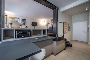 Et moderne køkken med indbygget mikroovn, et spiseområde med en stol, og en trappe op til en etage ovenover.