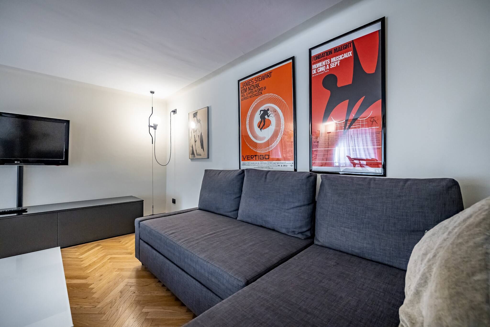 Un salon moderne avec un canapé gris, un téléviseur à écran plat et deux affiches accrochées au mur.