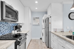 A modern kitchen with white cabinets, a stainless steel refrigerator, a coffee maker, and a clock on the wall. - Gulf-Front Condo | Panoramic Views | Marathon, FL (Marathon)