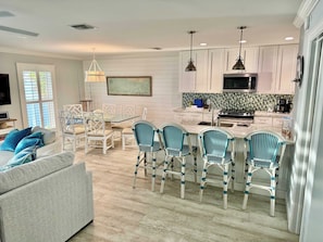 A modern kitchen with white cabinetry, a central island, and a dining area with wicker chairs. - Gulf-Front Condo | Panoramic Views | Marathon, FL (Marathon)