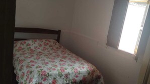 Ein kleines Zimmer mit einem Einzelbett, einer blumigen Tagesdecke, einem Holzkopfende und einem Fenster mit Blick nach draußen.