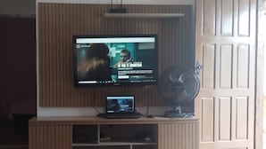 Ein Fernseher an einer Holzwand befestigt, darunter ein Laptop und ein Ventilator.