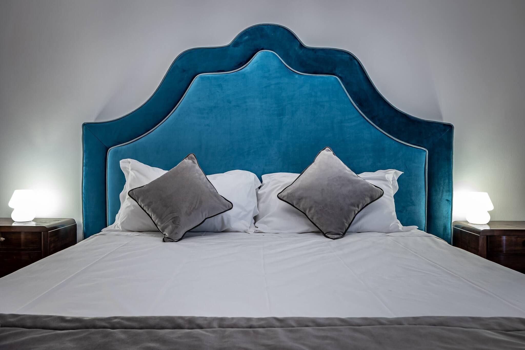 A bed with a teal upholstered headboard, white bedding, and two gray pillows.