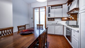 Una cuina amb armaris blancs, una taula de dinar de fusta i un paviment de rajoles.