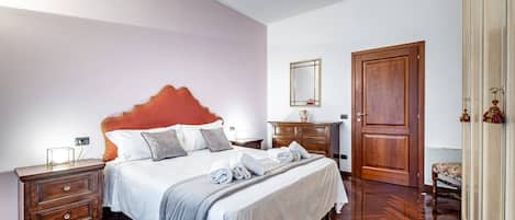 A bedroom with a large bed, wooden nightstands, a dresser, and a door.