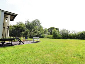 A grassy outdoor area with a bench, a chair, and a small structure with a roof. - Sid's Nest (Whitchurch)