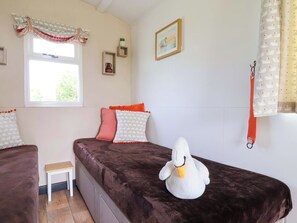 A bedroom with a bed, pillows, a small table, a window, a wall-mounted shelf, and a stuffed swan. - Sid's Nest (Whitchurch)