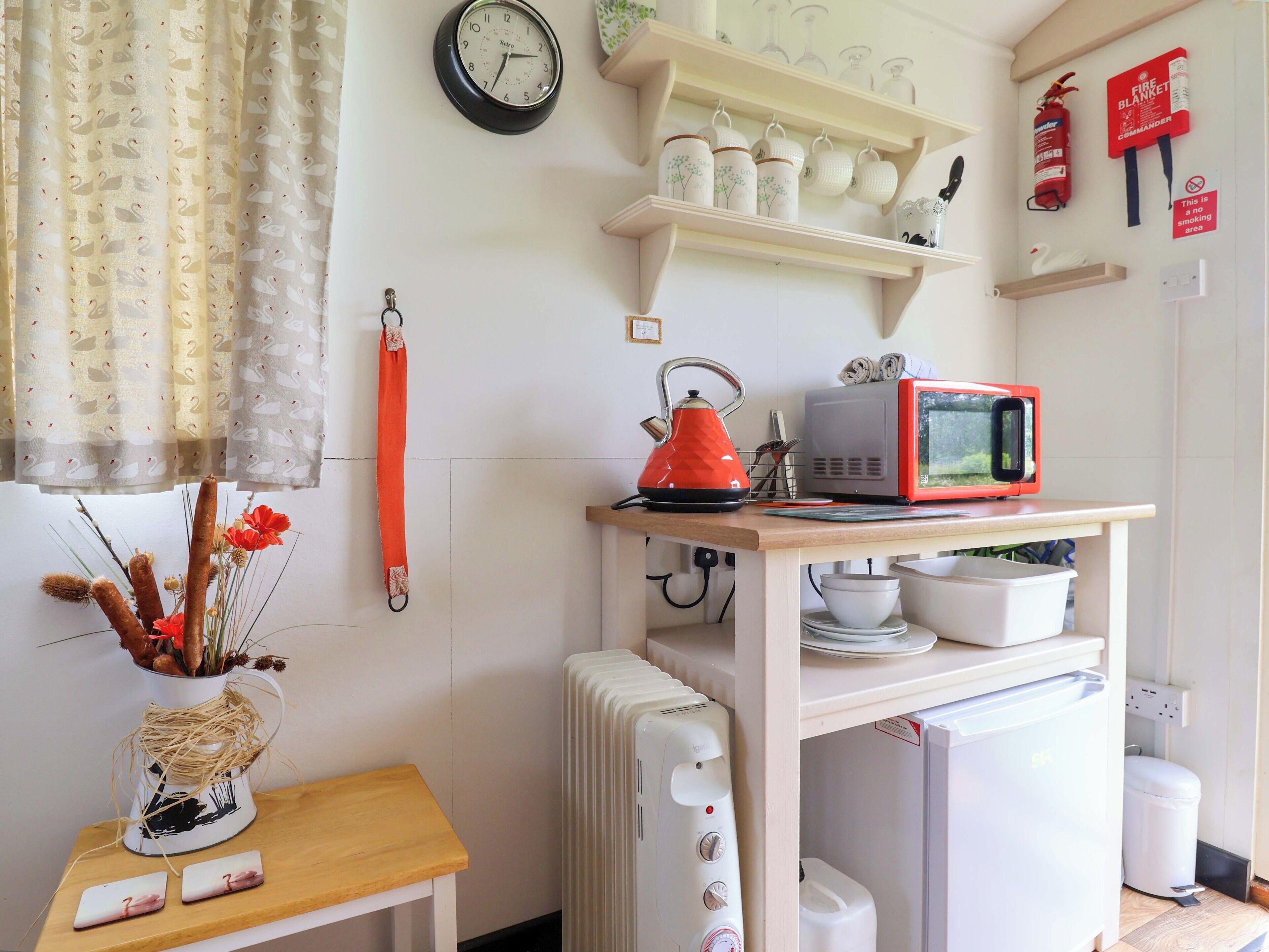 A compact kitchen with a microwave, kettle, and a small table with a vase.