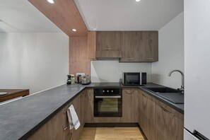 Eine moderne Küche mit Holzschränken, einer schwarzen Arbeitsplatte, einem Einbauofen, einer Mikrowelle und einem Spülbecken.