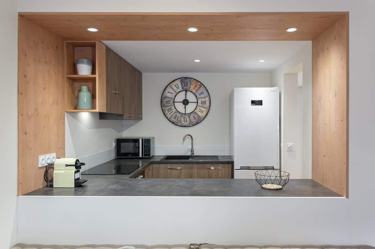 A compact kitchen with wooden cabinets, a microwave, a sink, and a decorative clock.