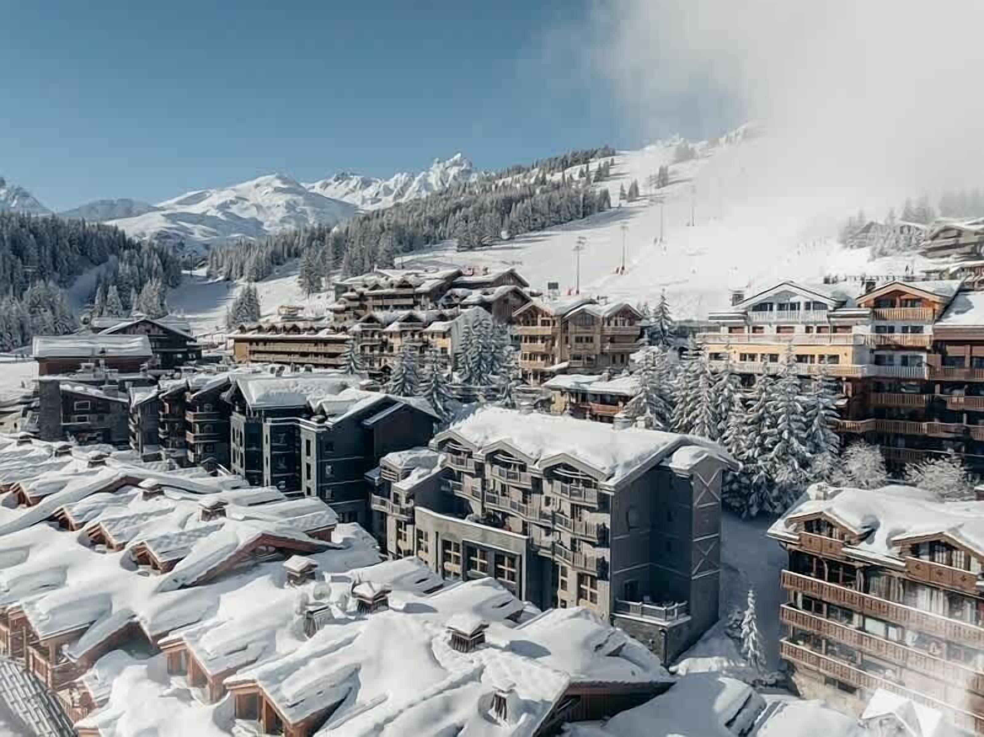 A snow-covered resort with multiple buildings, including lodges and hotels, with a mountainous backdrop.