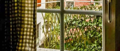 A window with a metal frame, a view of a brick building, and a green hill in the background.