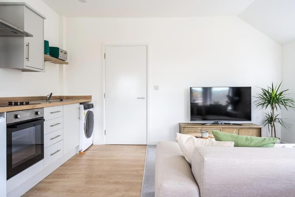 A compact living space with a kitchenette, a washing machine, a flat-screen TV, and a bed.